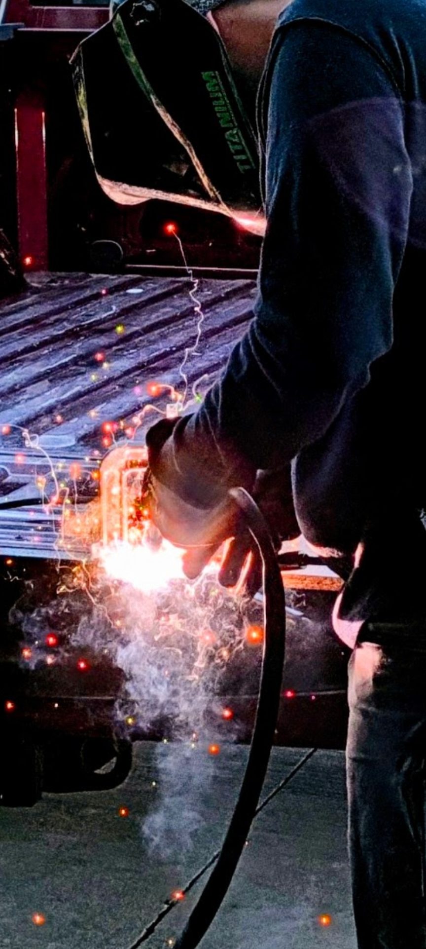 Precision Trailer Solutions welding a truck bed on-site, sparks flying